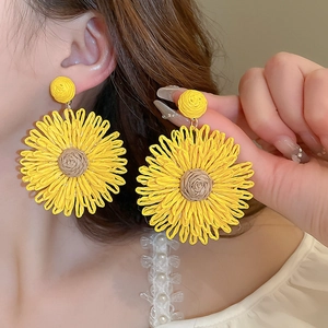 Detailed view of handmade yellow sunflower woven earrings worn by a female model