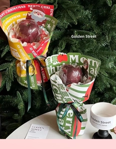 Close-up of Christmas kraft paper gift packaging for apples with festive ribbon and tree background