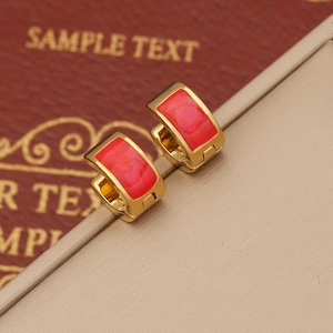 Close-up of gold geometric earrings featuring rectangular red enamel stones on leather
