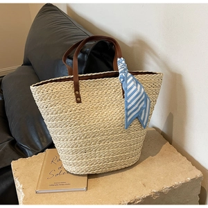 Detail of straw tote bag with brown leather handles and a blue striped silk scarf