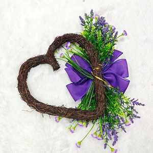 Heart-shaped vine wreath with purple bow and artificial greenery on white fur background