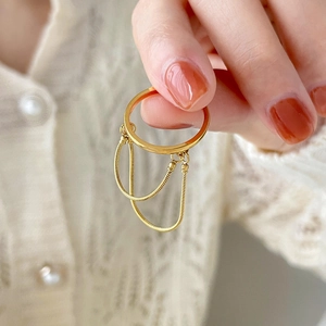Golden titanium steel twist ring with double snake chain tassels held against lace fabric