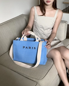 Detailed view of blue straw tote bag with PARIS embroidery and woven texture