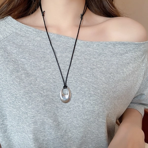 Gros plan d'un collier pendentif ovale en argent avec cordon noir porté au cou