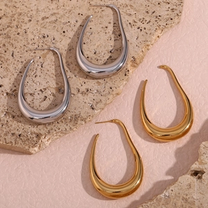 Polished hollow curve earrings in gold and silver finish on textured stone backdrop