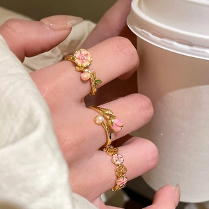 Detailed view of floral enamel rings and pearl gold rings worn by a model on hand