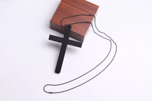 Detail of vintage black wooden cross pendant on a metal ball chain over a wood block