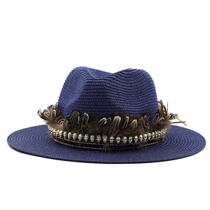 Detail of navy straw fedora hat featuring brown feathers and silver skull charms