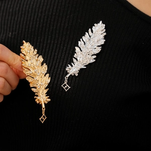 Close-up of gold and silver leaf feather brooches with rhinestones on black fabric