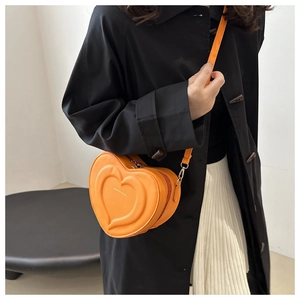 Detail of a chic orange heart-shaped crossbody bag with embossed patterns and adjustable strap