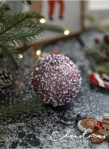 Macro detail of 8cm purple sequin and white pearl Christmas ball hanging on a festive tree