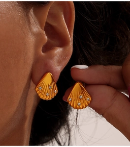 Close-up of elegant gold shell-shaped earrings with diamond inlay on model ear