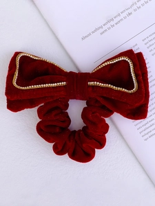 Detailed view of a red velvet hair bow with sparkling gold rhinestones on white background