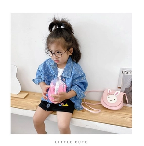 Girl sitting on a bench wearing a cute pink rabbit crossbody bag and denim jacket