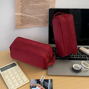 Dual-layer red nylon pencil case with metal zipper on a wooden desk setup