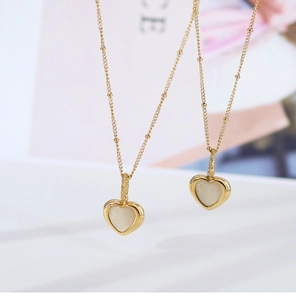 Macro view of gold heart necklace featuring iridescent white shell insets on a bead chain