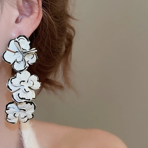 Detail of elegant three-tier floral drop earrings with white enamel finish on model