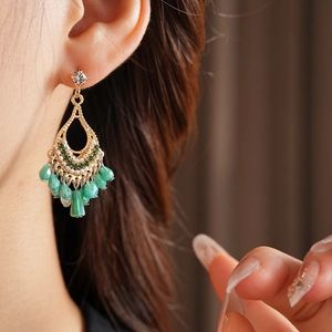 Close-up of golden teardrop tassel earring with green crystals on a model