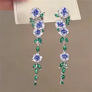 Macro detail of long floral drop earrings with blue enamel petals and green leaf accents