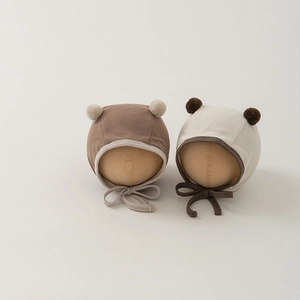 Detailed view of two knit baby earflap hats with pom-poms and adjustable chin ties