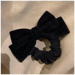 Detailed view of black velvet bow hair scrunchie with soft fabric texture on beige background