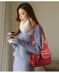 Close-up of a red soft leather crossbody bag with multiple zippers shown on a model