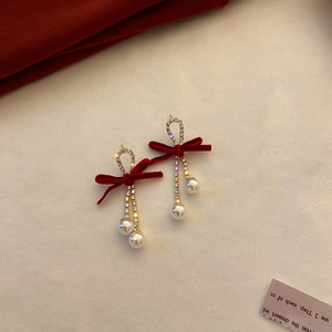 Detail of red velvet bow earrings with sparkling crystal chains and elegant round pearls