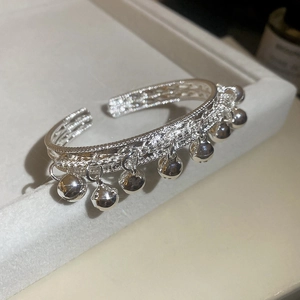 Détail d'un bracelet ouvert argenté avec clochettes et texture tissée sur un support