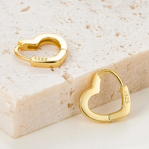 Close-up of golden S925 sterling silver heart earrings on a textured stone base