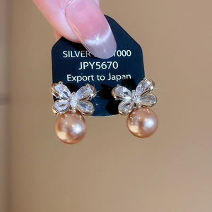 Macro view of bow-shaped zircon stud with a champagne gold pearl drop earring