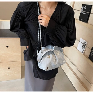 Detail of light blue pleated bucket bag featuring 3D metal butterfly and chain strap