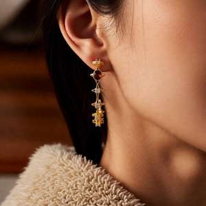 Close-up of 18k gold plated C-shaped earrings with tiger eye stone on ear