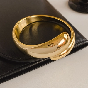 Macro detail of glossy gold wrap bracelet with minimalist sculptural ends on dark background