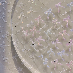 Macro detail of 3D iridescent bow nail art stickers with delicate rhinestones and text