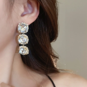 Close-up of triple halo crystal drop earrings in gold finish worn by a model
