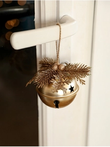 Close-up of golden Christmas bell with star cutouts and pine needle detail on a door