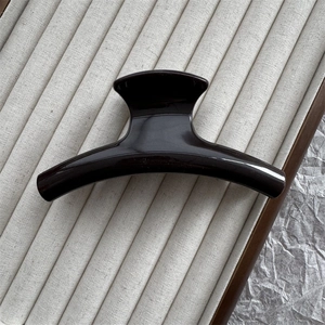 Close-up of a 11cm curved black hair claw clip with a glossy finish on textured fabric