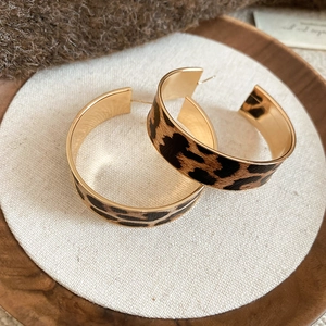 Close-up of leopard print C-shape hoop earrings on a minimalist wooden display tray
