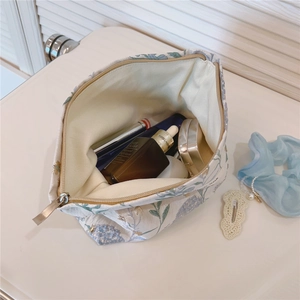 Detail showing internal capacity of the floral canvas makeup bag with various cosmetics