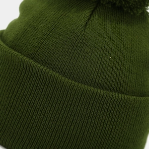 Close-up of dark green ribbed knit winter beanie featuring a soft matching pom-pom detail