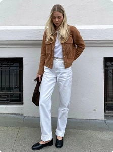 Estilo callejero de mujer con chaqueta de ante marrón, vaqueros blancos y bolso de mano
