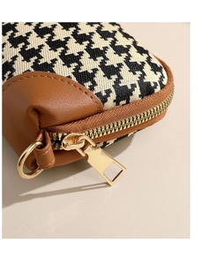 Close-up of black and white houndstooth fabric with premium gold zipper and leather trim