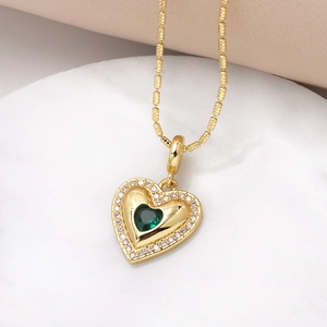 Gold heart necklace with an emerald green gemstone and white zircon stones on marble