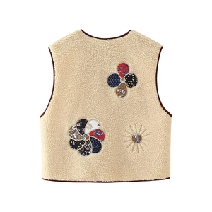 Detail of floral patch embroidery on beige faux shearling vest with brown trim
