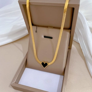 Detail of a gold snake chain necklace featuring a black heart pendant on white fabric