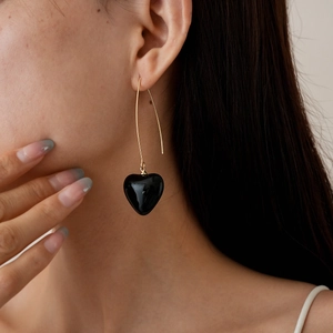 Close-up of elegant gold hook earrings with glossy black heart pendants on a model