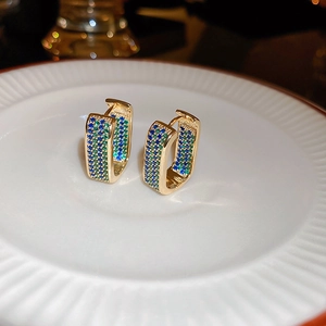 Macro shot of U-shaped gold earrings with blue and green pave-set cubic zirconia