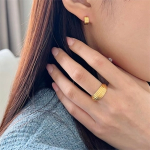 Detail shot of golden multi-layer ridged ring and matching hoop earrings on model