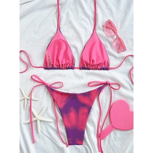 Flat lay of pink and purple tie-dye string bikini with beach accessories on white fabric