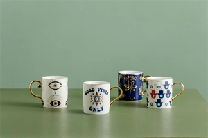 Set of four ceramic coffee mugs with gold handles featuring mystic hand and evil eye motifs